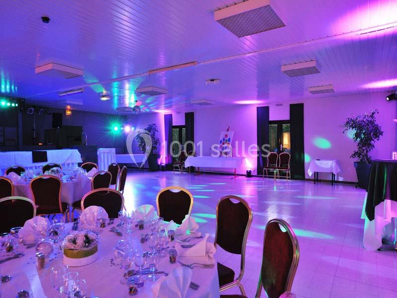 Salle de réception décorée avec des tables dressées, éclairage coloré et ambiance festive.