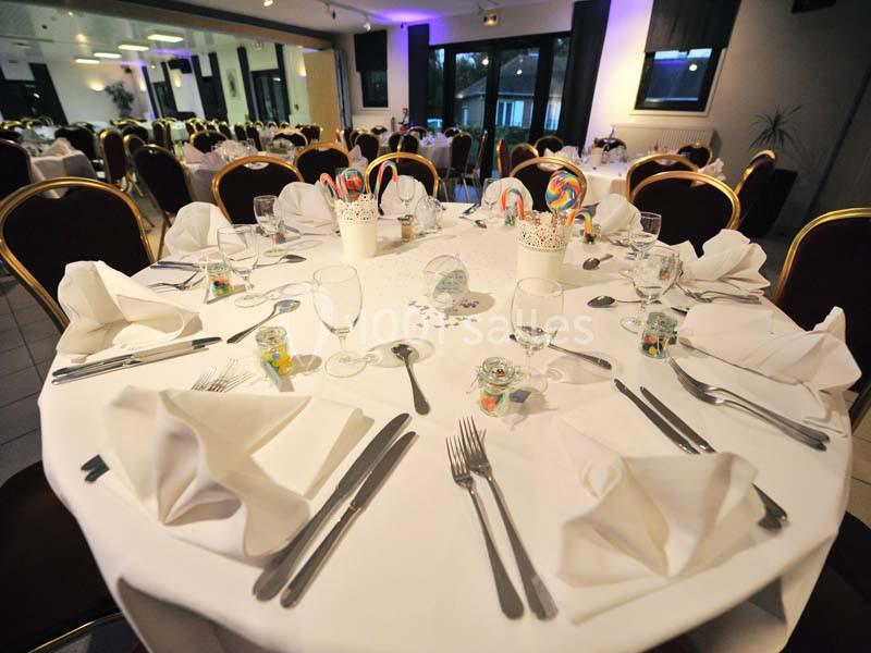 Salle de réception avec tables rondes dressées, nappes blanches, couverts disposés et décorations colorées.
