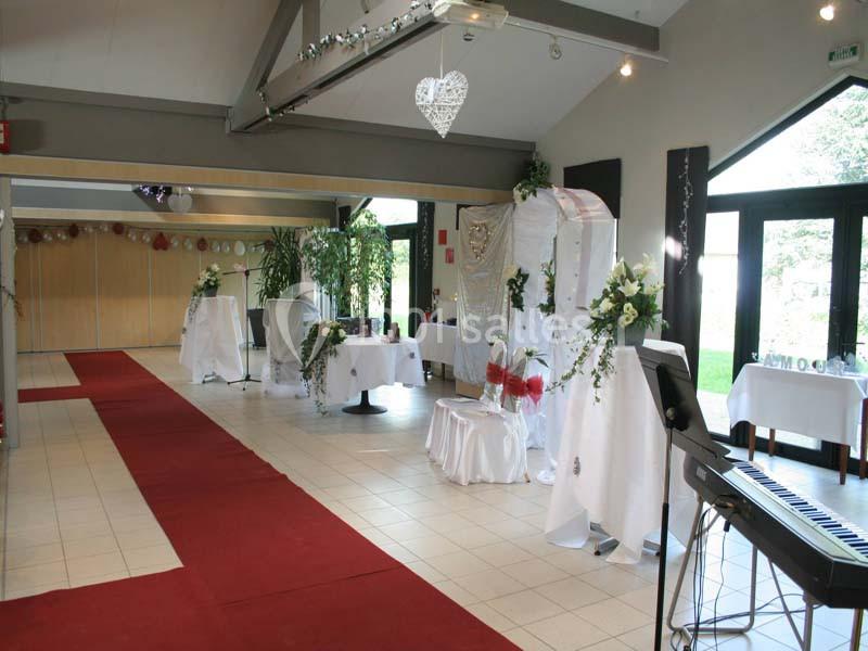 Salle décorée pour un événement avec nappes blanches, fleurs, tapis rouge et lumière naturelle entrant par les baies vitrées.
