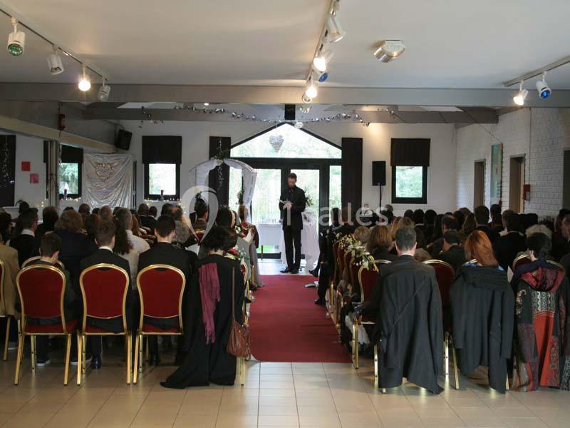 Cérémonie dans une salle avec des invités assis sur des chaises rouges, face à un orateur devant une arche décorée.