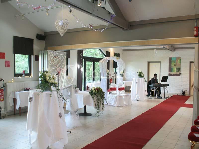 Salle décorée pour un mariage avec des tables drapées de blanc, un tapis rouge et un pianiste jouant en arrière-plan.