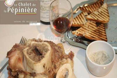 Assiette d'os à moelle avec pain grillé, verre de vin rouge et sel, posés sur une table avec une bouteille en arrière-plan.