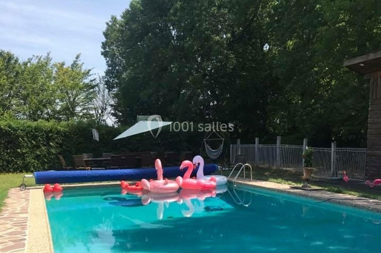 Piscine extérieure avec des bouées flamants roses flottant sur l'eau, entourée de verdure et d'une terrasse.