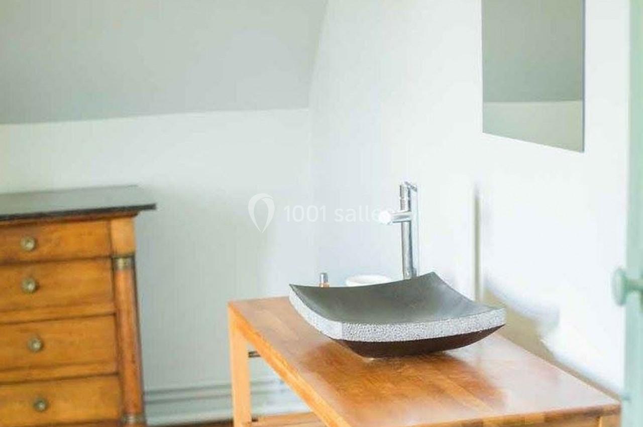 Lavabo moderne en pierre sur une table en bois, avec un miroir et une commode en arrière-plan dans une pièce lumineuse.