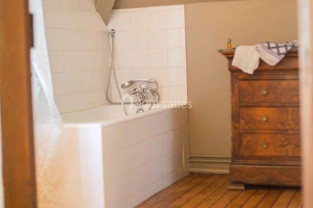 Baignoire blanche avec pomme de douche, située dans une salle de bain avec parquet et commode en bois.