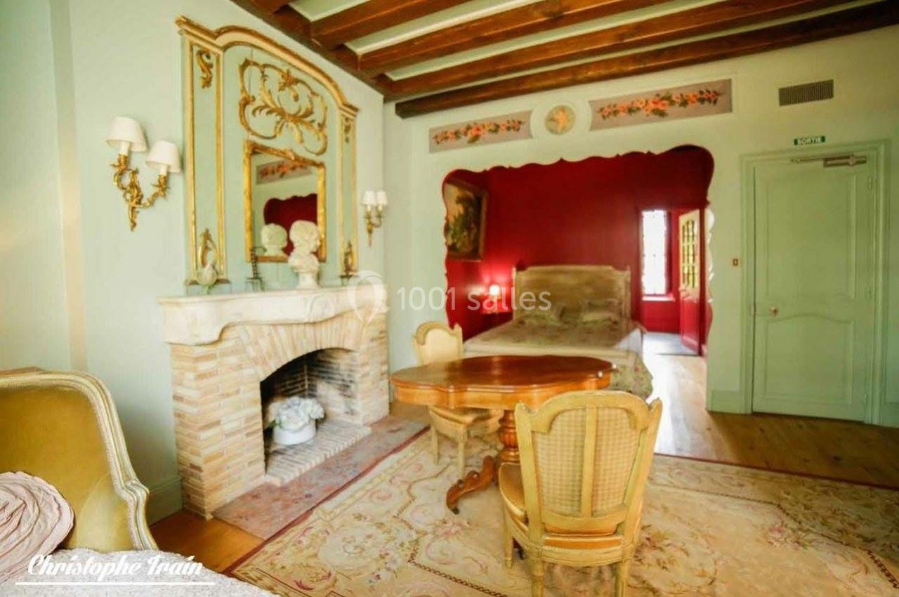 Chambre décorée de style classique avec cheminée en pierre, mobilier en bois et lit encadré par un mur rouge.