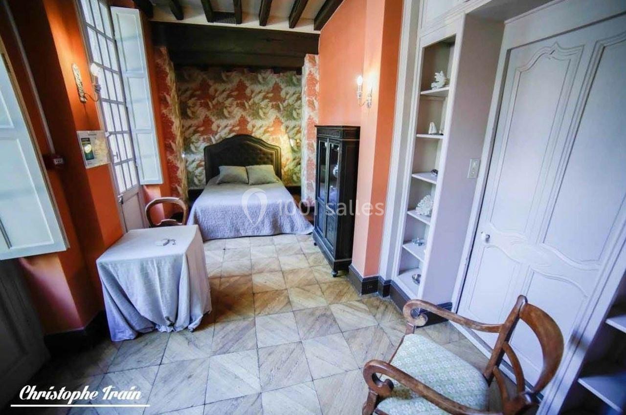 Chambre lumineuse avec lit double, murs orange, armoire noire, table et chaise en bois, sol en carrelage clair.