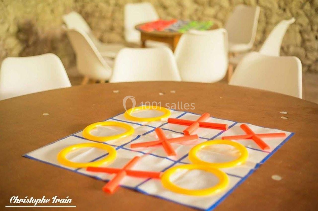 Jeu de morpion avec des pièces en plastique colorées sur une table ronde, des chaises blanches en arrière-plan.