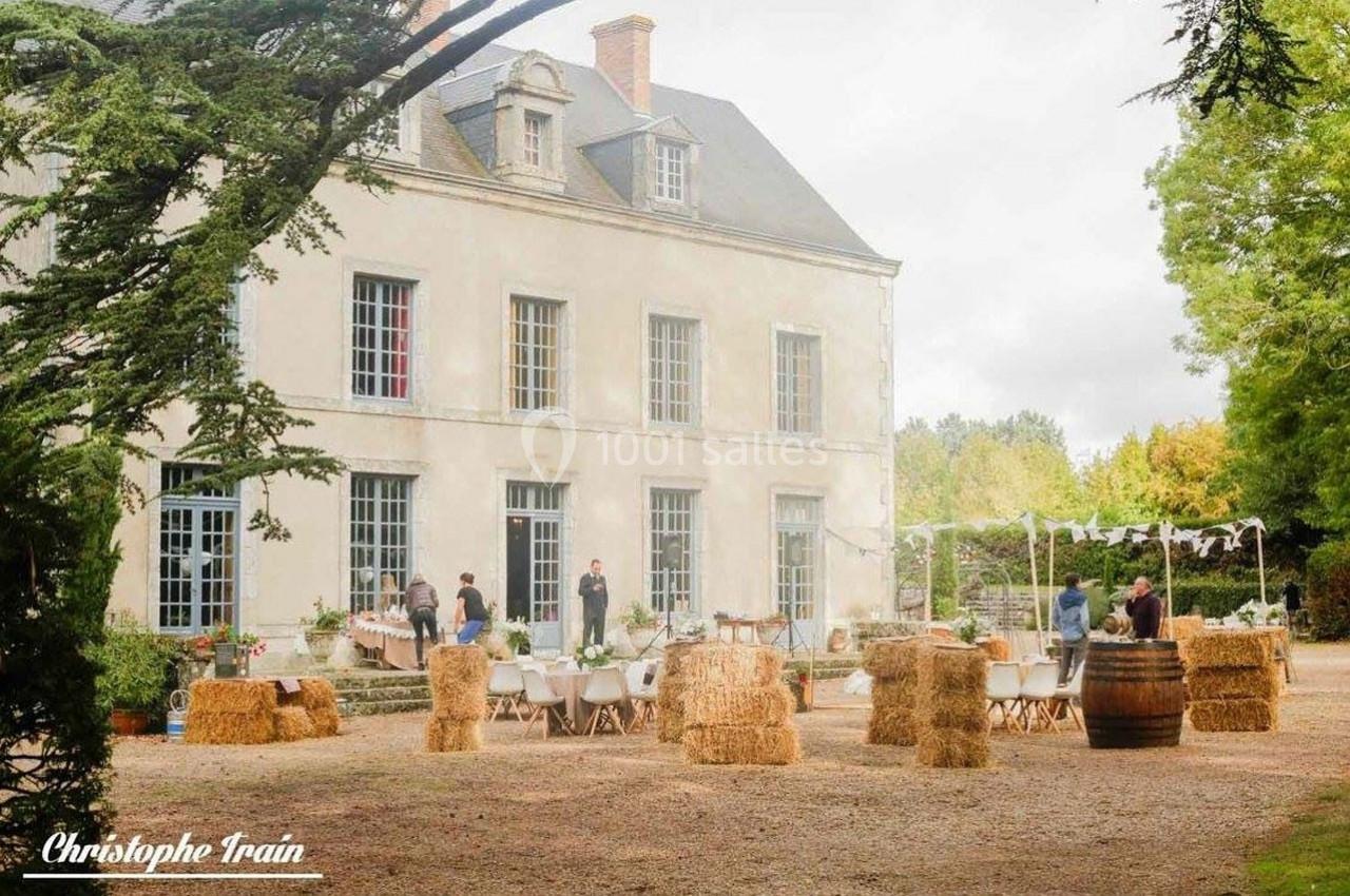 Façade d'un manoir avec une cour aménagée pour un événement, décorée de bottes de paille et de tables.