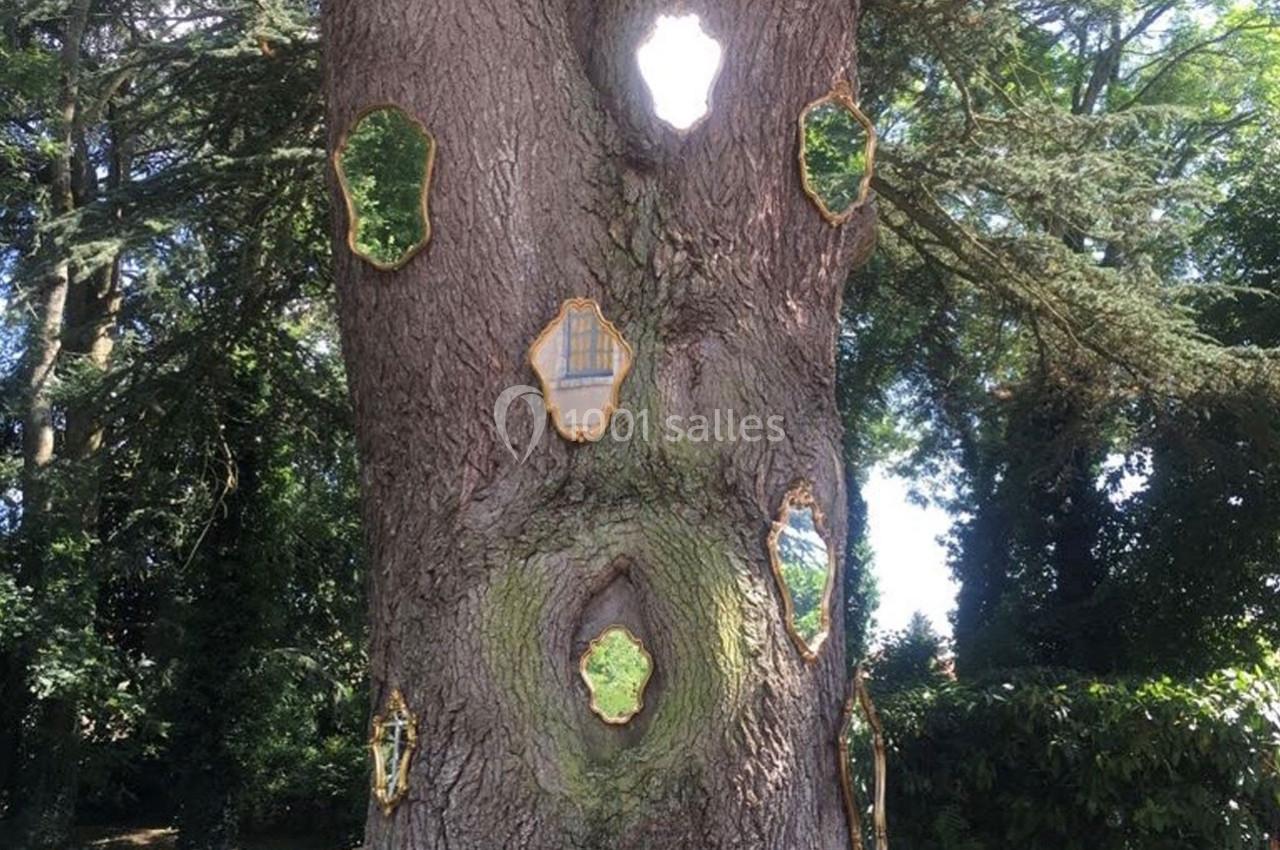 Arbre avec des miroirs dorés intégrés dans son tronc, reflétant la lumière et le paysage environnant.