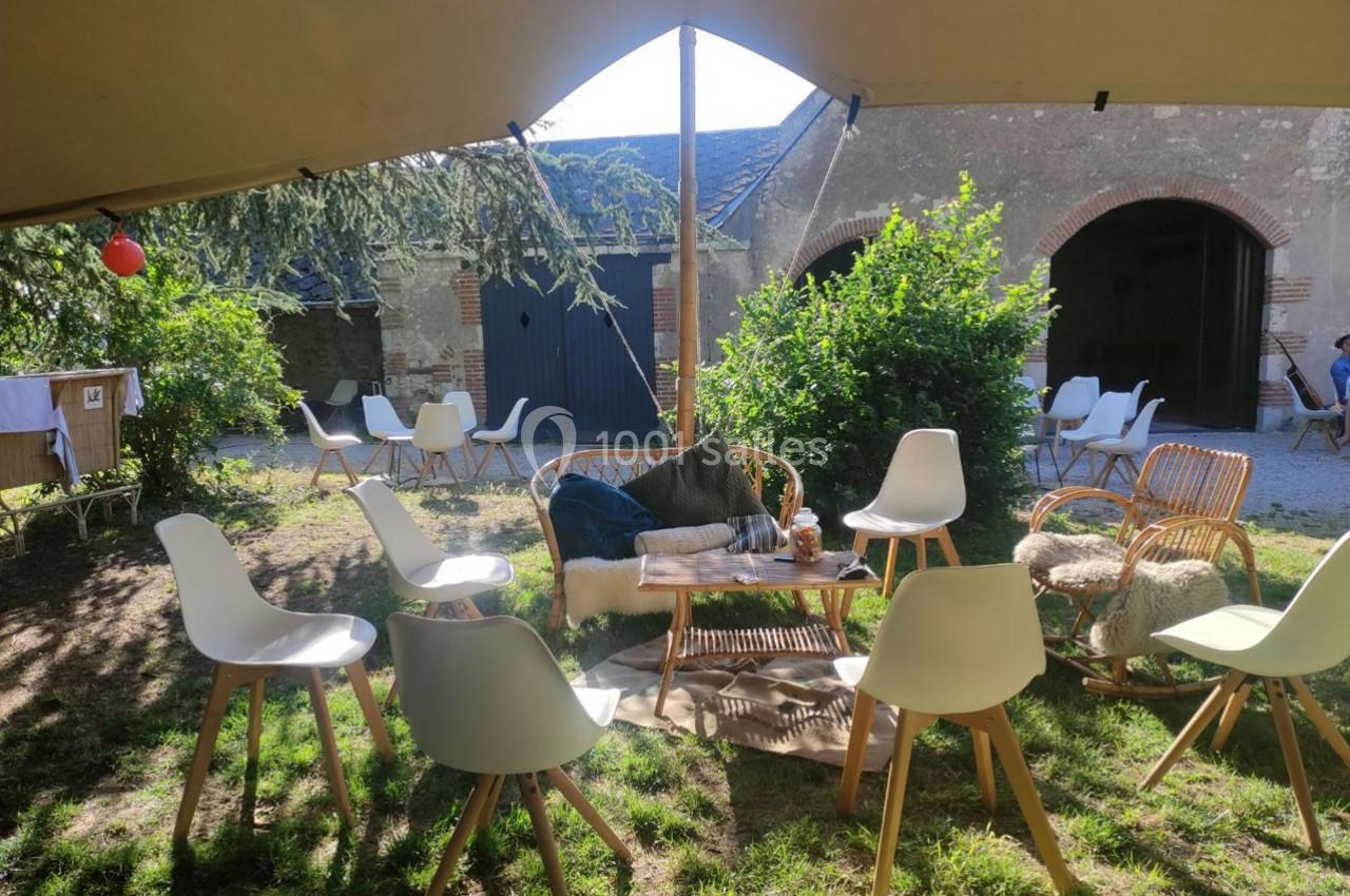 Chaises et tables disposées en cercle sous une tente dans un jardin, avec des bâtiments en arrière-plan.