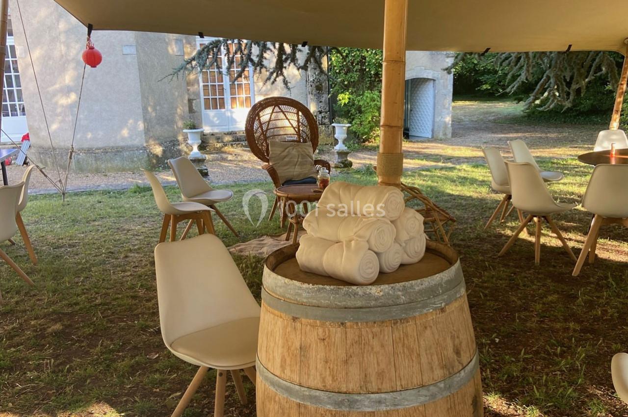 Des serviettes roulées posées sur un tonneau en bois sous une tente, entourées de chaises et d'un fauteuil en osier.