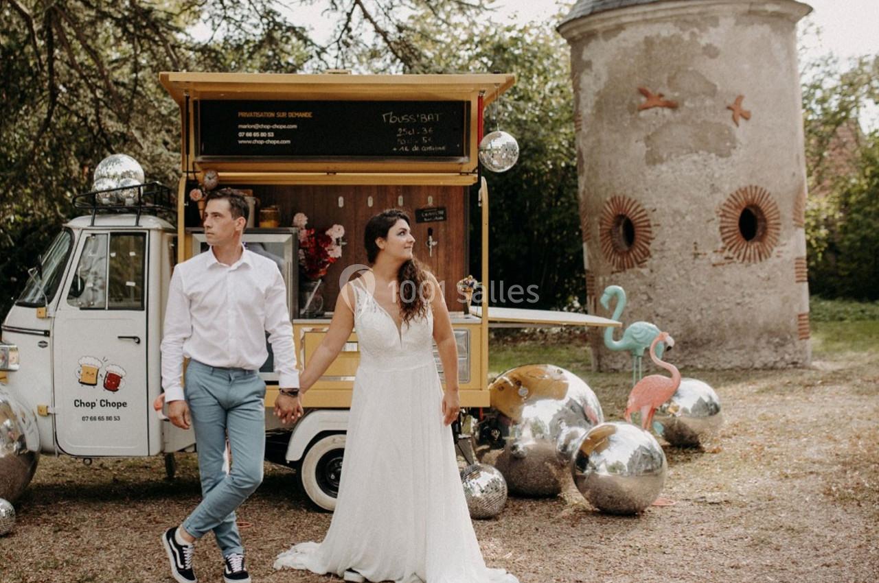 Un couple en tenue de mariage pose devant un food truck et des décorations extérieures avec des flamants roses et des…