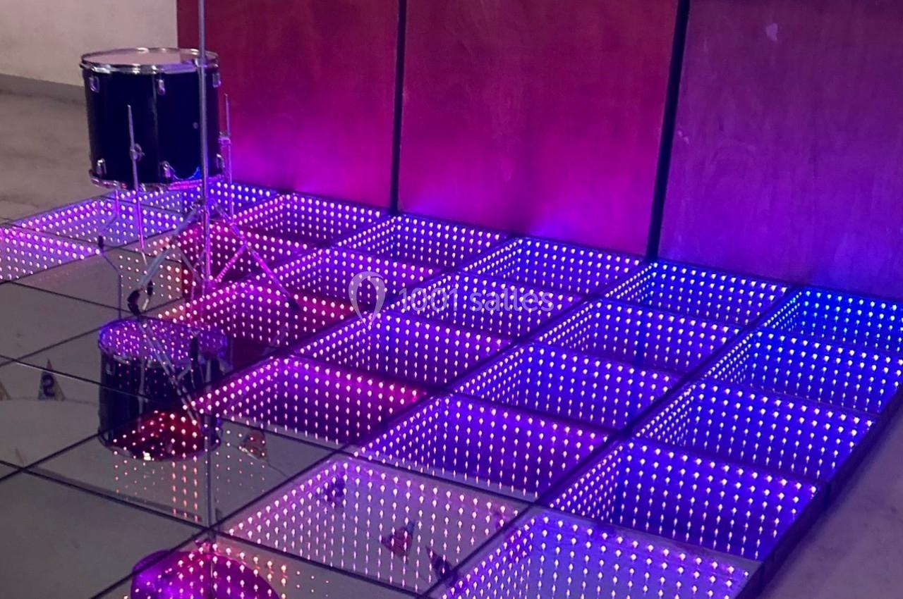 Scène avec un sol lumineux à carreaux LED violets et un tambour installé à côté d'un mur en bois.