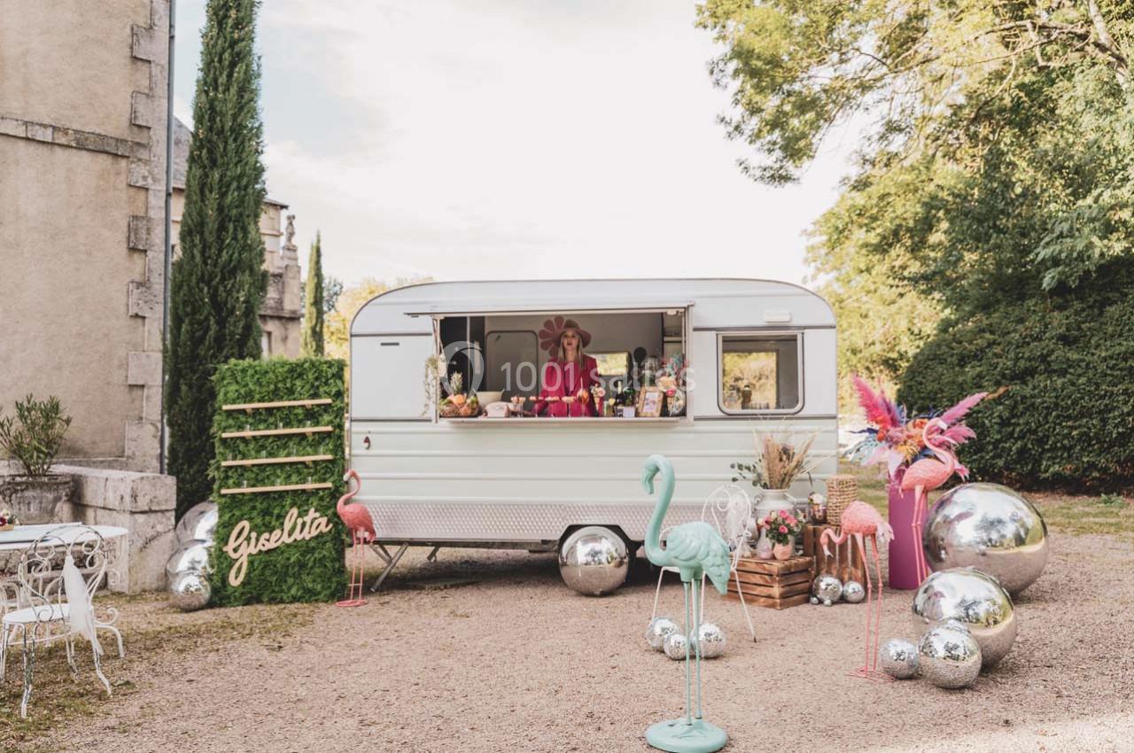 Caravane vintage aménagée en stand, entourée de décorations colorées, flamants roses et boules argentées.