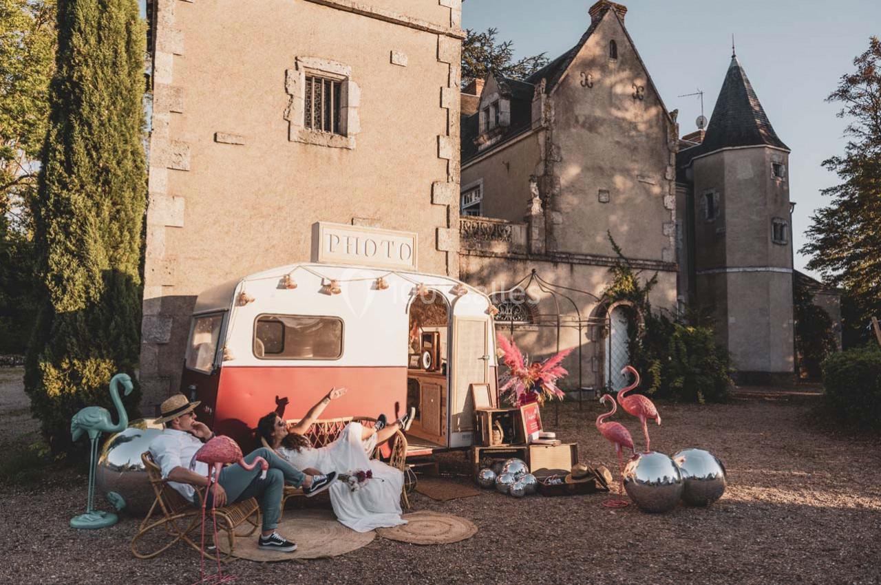Une caravane rétro aménagée en photobooth devant un château, entourée de décorations festives et de flamants roses.