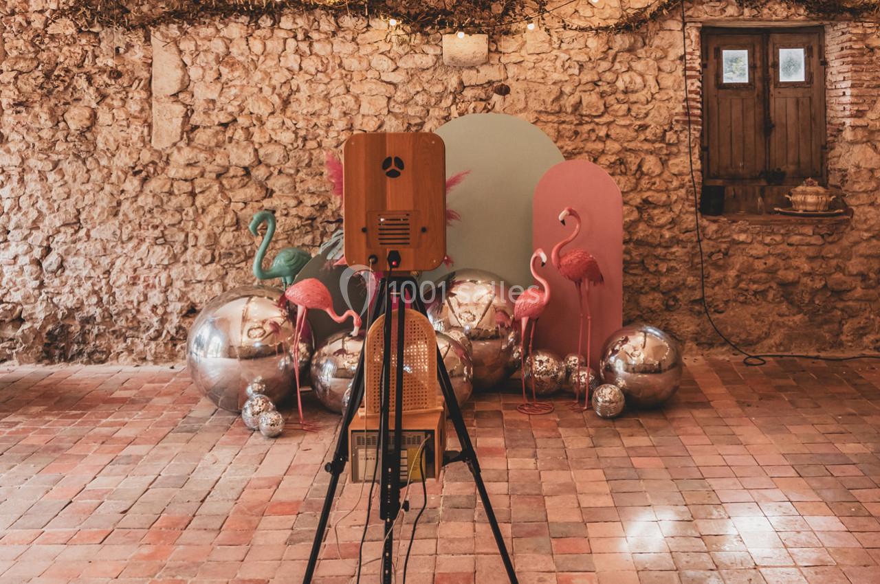 Trépied avec appareil photo devant une décoration colorée composée de flamants roses, sphères argentées et panneaux pastel.