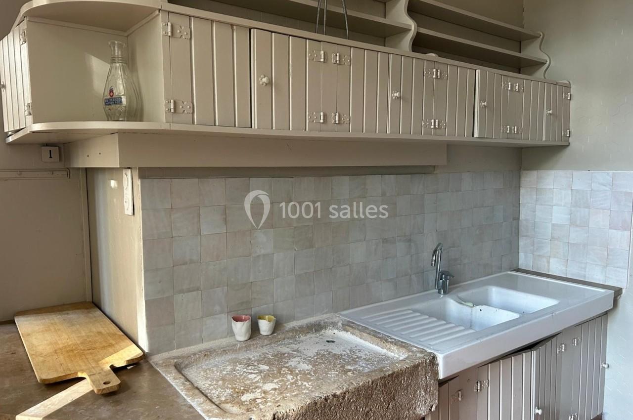 Cuisine ancienne avec évier en pierre, plan de travail usé, crédence carrelée et placards en bois clair.