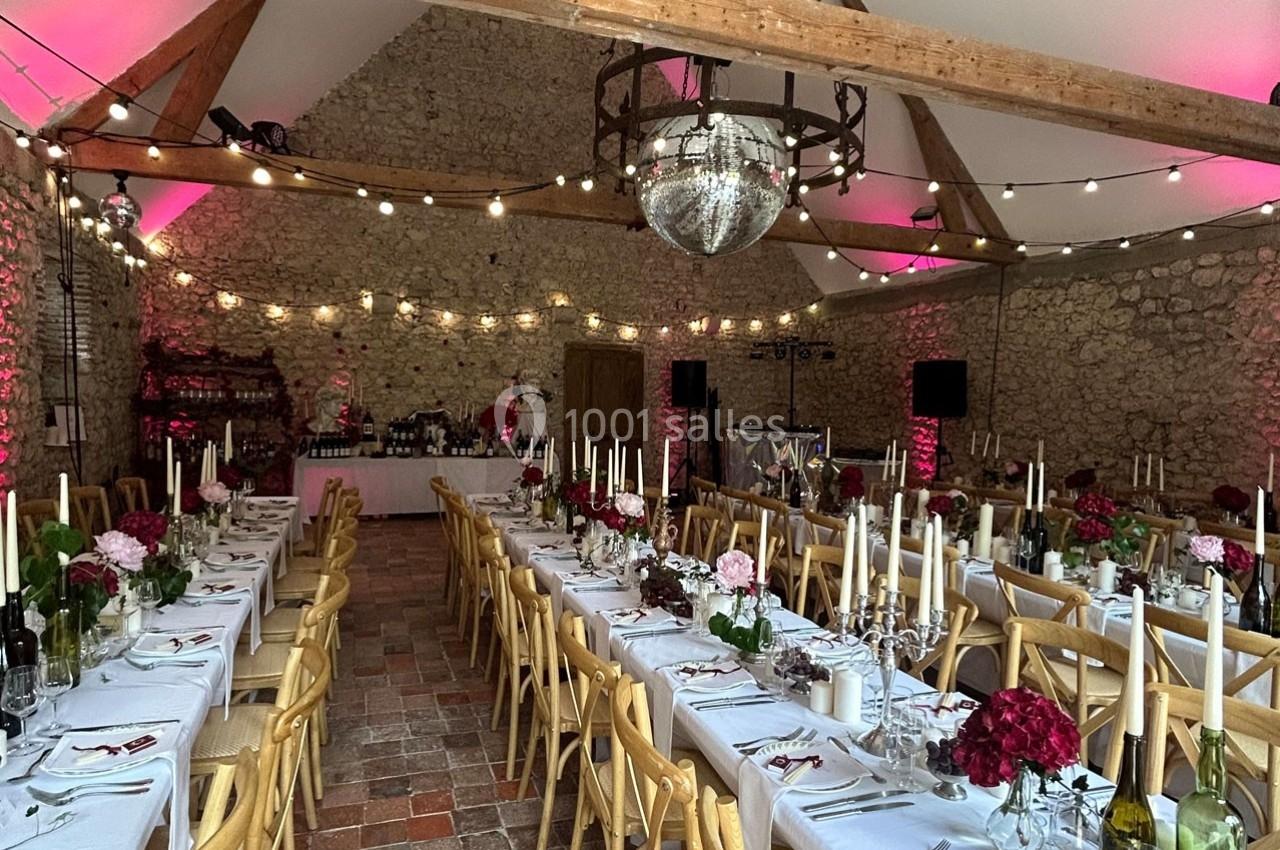 Salle de réception en pierre avec tables décorées, chandeliers, fleurs et guirlandes lumineuses suspendues.