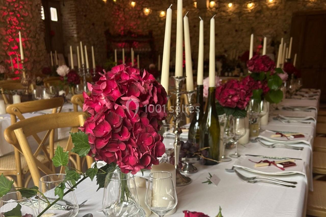 Table décorée pour un dîner avec des bouquets d'hortensias roses, chandeliers et vaisselle élégante dans une salle en pierre.