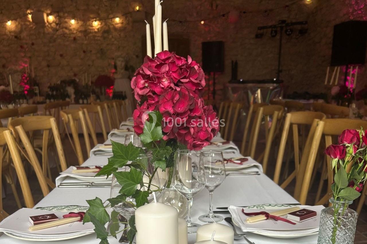 Salle de réception décorée avec des tables dressées, des bougies blanches et des bouquets de fleurs rouges.