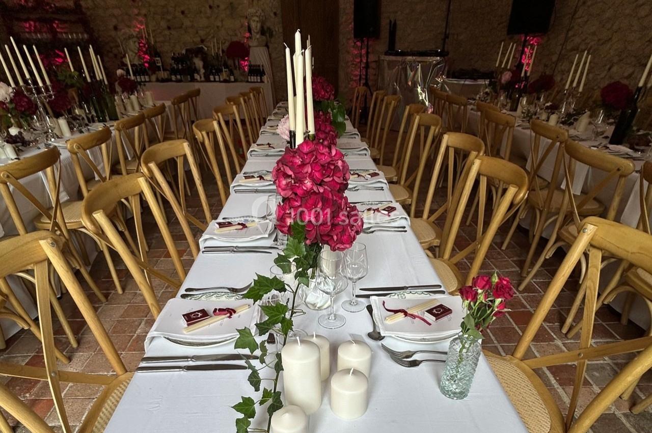 Tables de réception décorées avec des bougies, des fleurs rouges et du lierre, dans une salle en pierre.