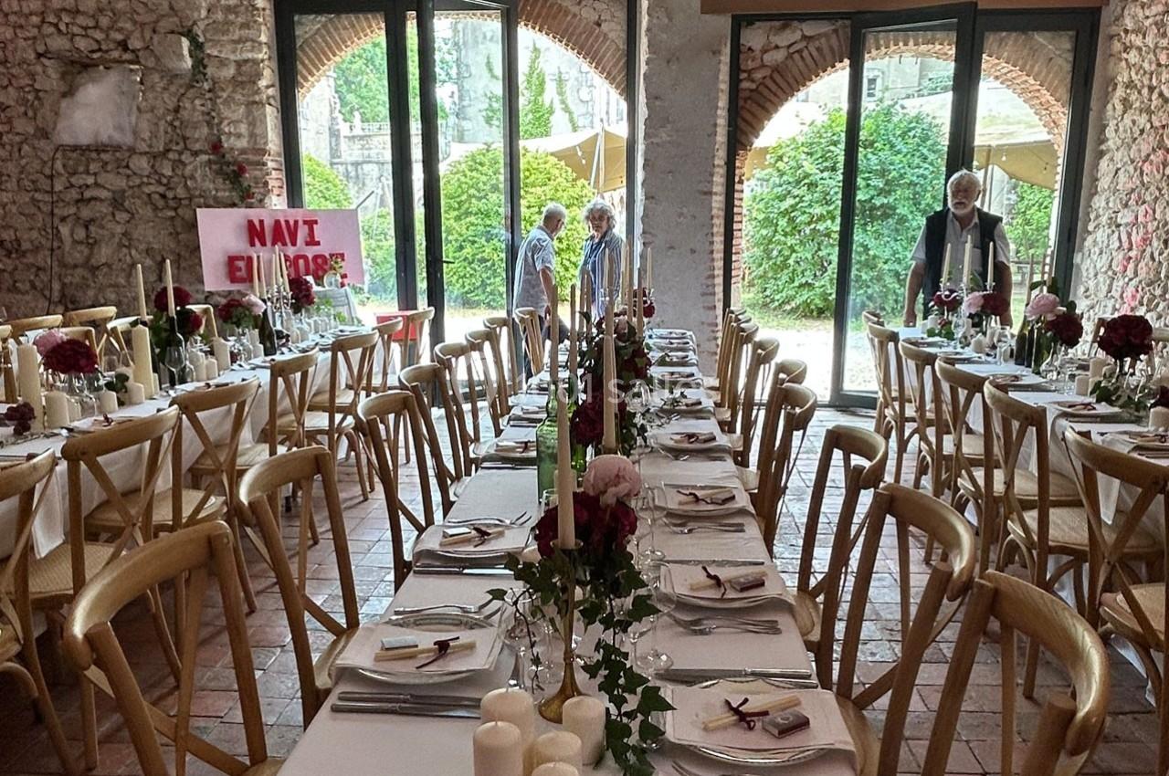 Salle de réception décorée pour un mariage avec longues tables dressées, bougies et fleurs, ouverte sur un jardin.