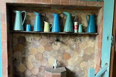 Façade d'une maison ancienne en pierre avec des fenêtres à petits carreaux, entourée de végétation.
