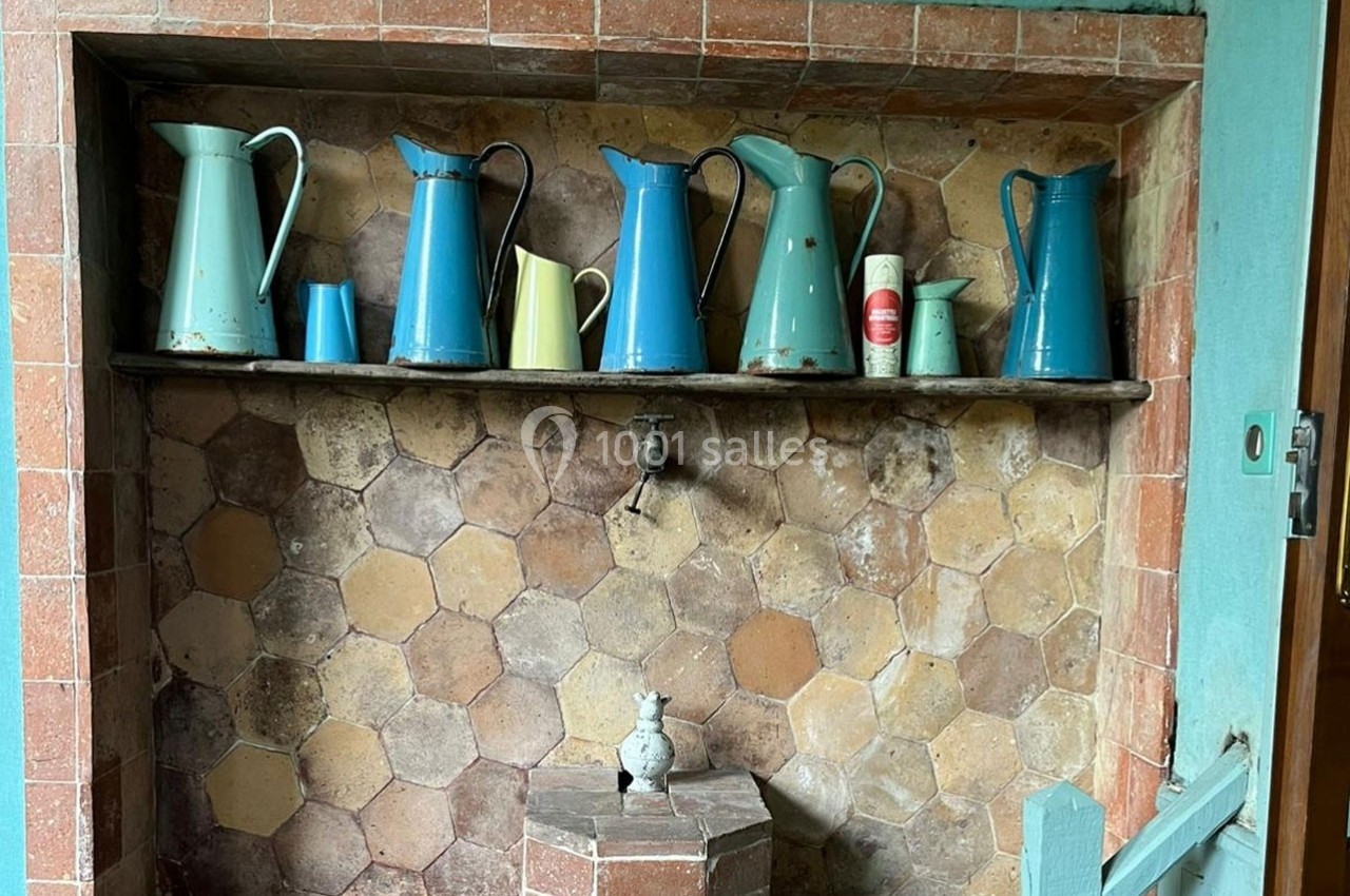 Collection de pichets en métal colorés alignés sur une étagère dans une niche murale en carreaux anciens.