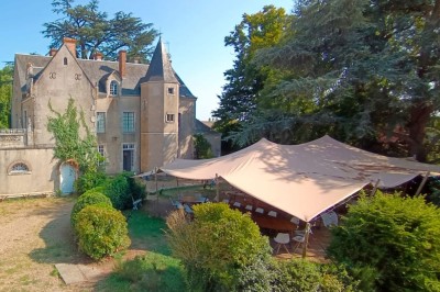 Façade d'une maison ancienne en pierre avec des fenêtres à petits carreaux, entourée de végétation.