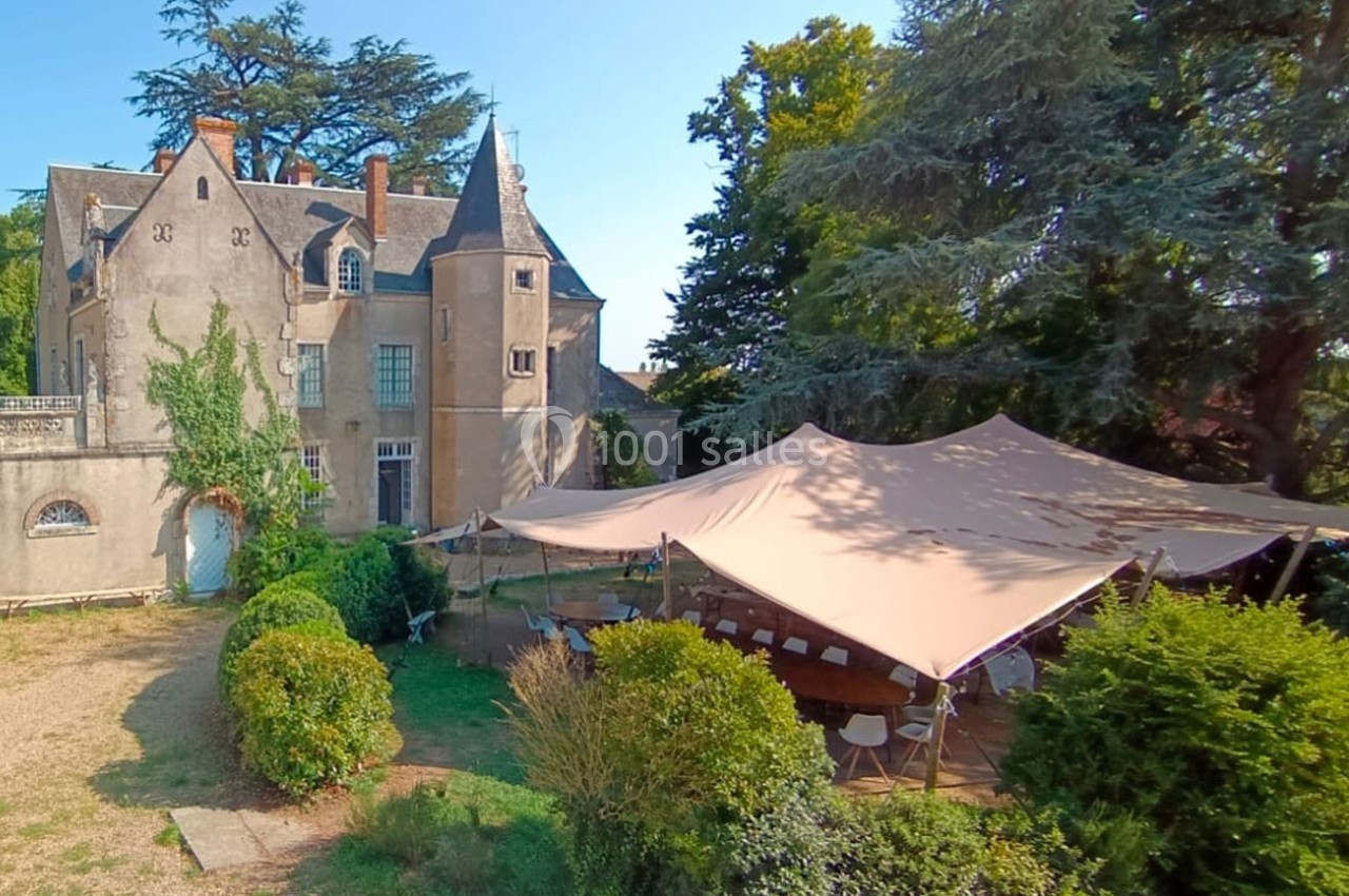 Château ancien entouré de verdure avec une grande tente installée pour un événement en extérieur.