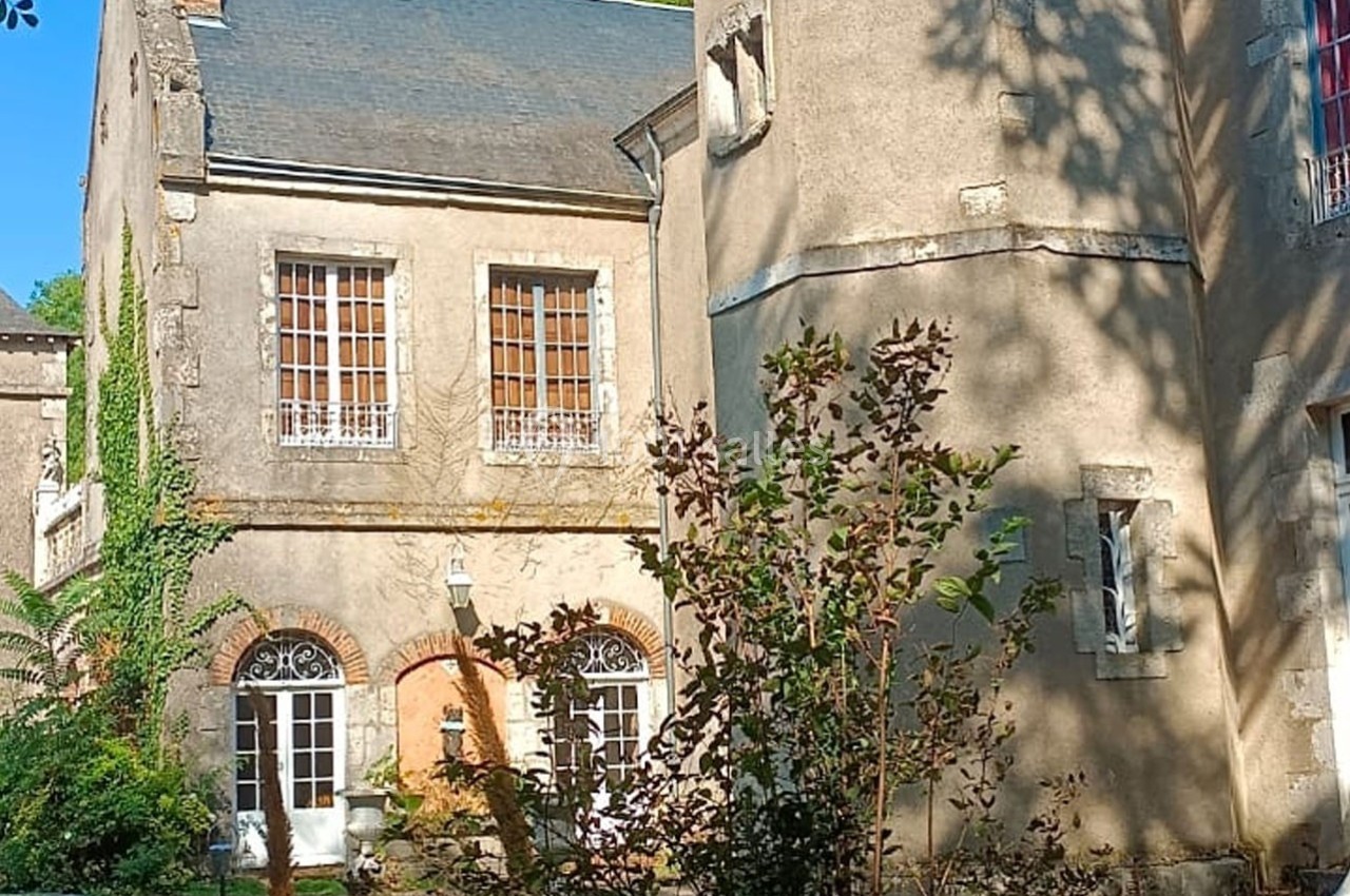 Façade d'une maison ancienne en pierre avec des fenêtres à petits carreaux, entourée de végétation.