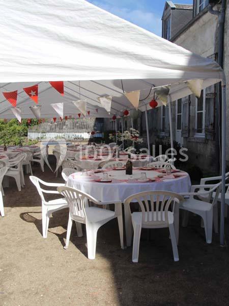 Tables rondes dressées sous une tente blanche avec des guirlandes de fanions, entourées de chaises en plastique blanc.