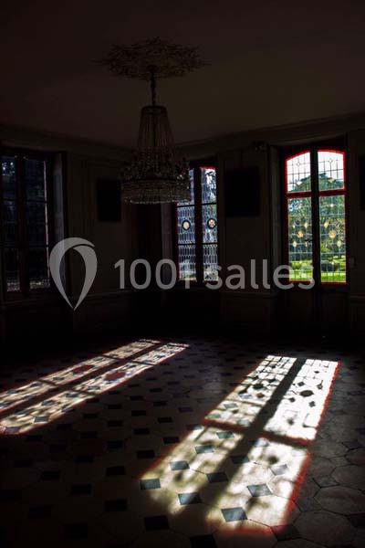 Lumière naturelle traversant des vitraux colorés, projetant des motifs sur un sol carrelé dans une pièce sombre.