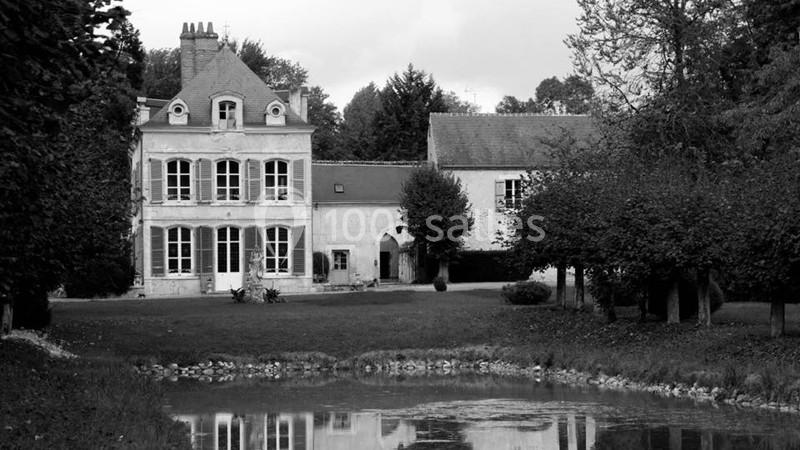 Manoir ancien entouré d'arbres, avec une pelouse et un étang au premier plan.