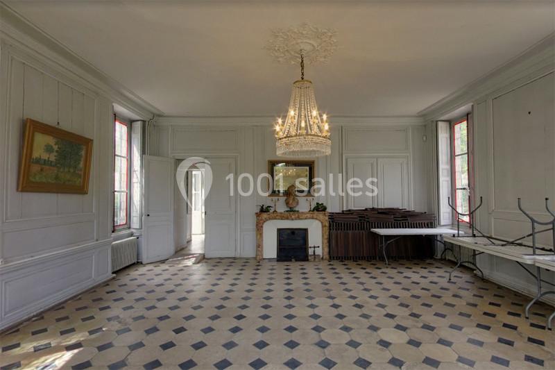 Salle lumineuse avec carrelage en damier, cheminée ornée d'un miroir, lustre central et tables pliées contre les murs.