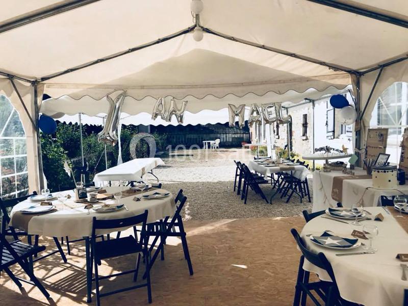 Intérieur d'une tente décorée pour une fête, avec des tables dressées et des ballons formant le texte ’1 an’.