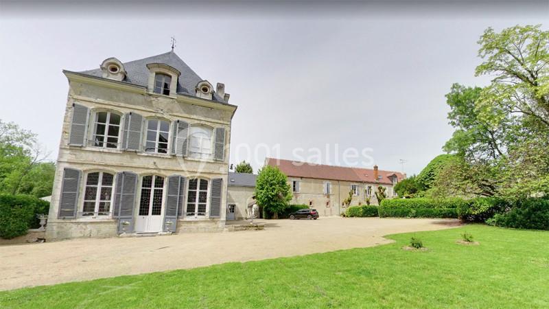 Maison ancienne en pierre avec volets gris, située dans un grand jardin verdoyant, accompagnée d'un bâtiment annexe.