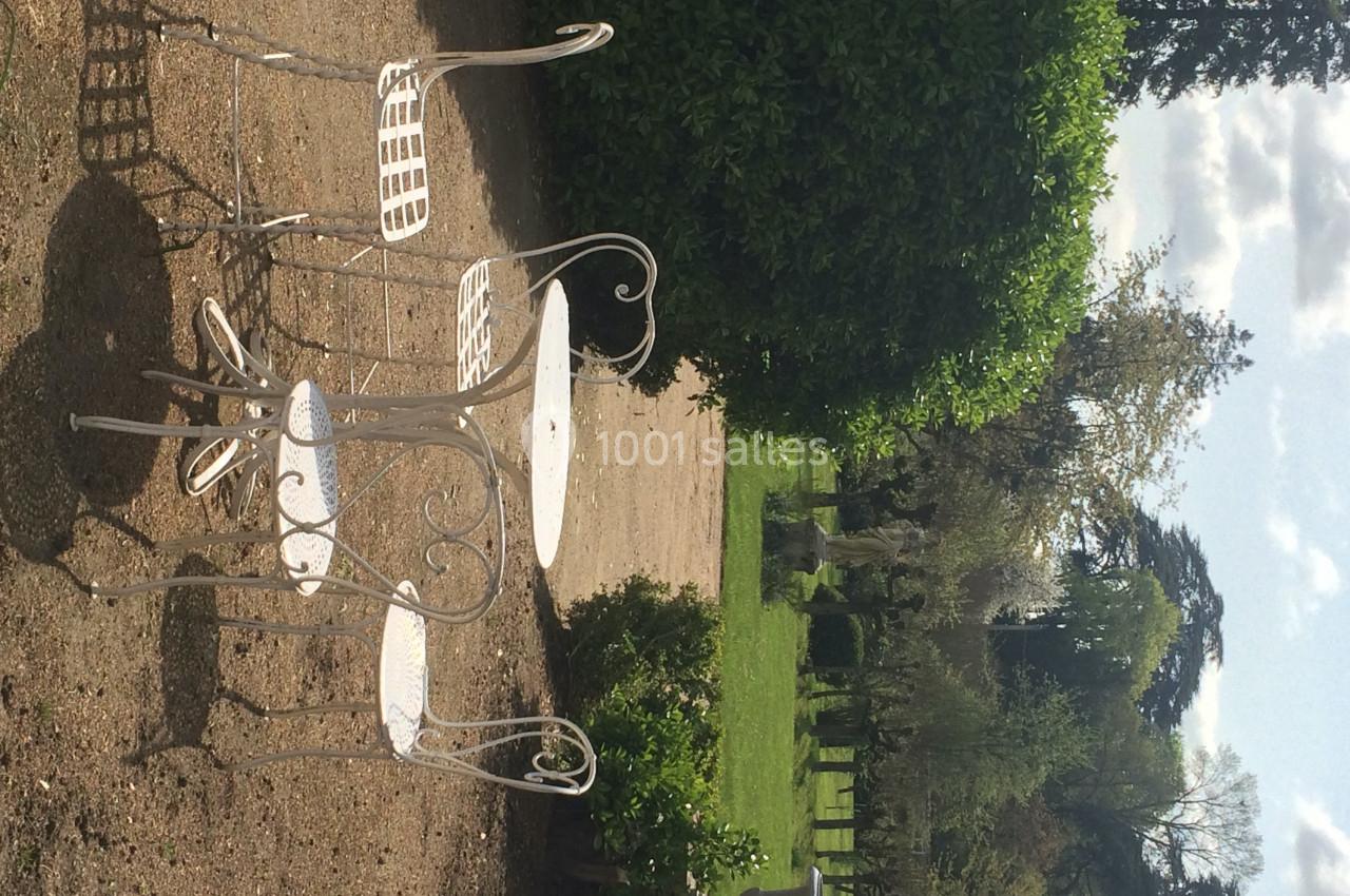 Mobilier de jardin en fer forgé blanc sur une terrasse en gravier, entouré de verdure et d'arbres.