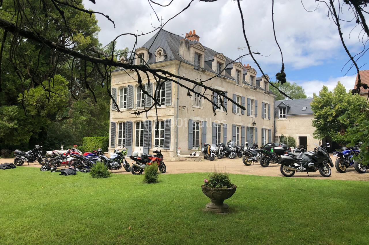 Façade d'un grand bâtiment ancien entouré de motos stationnées sur une pelouse et une allée gravillonnée.