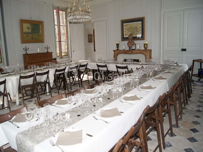 Salle élégante avec tables dressées pour un repas, nappes blanches, chaises en bois et décorations classiques.