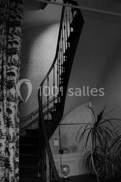 Escalier en bois sombre avec une rampe en fer forgé dans un intérieur ancien, éclairé par une lumière douce.