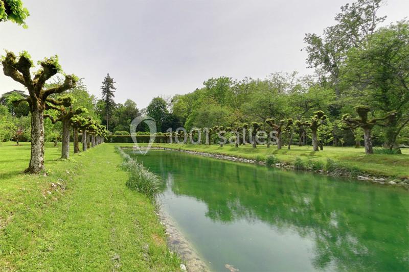 Allée bordée d'arbres taillés et d'un canal d'eau calme dans un parc verdoyant.