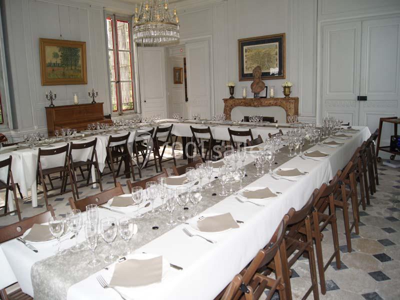 Salle élégante avec de longues tables dressées, nappes blanches, verres et serviettes, prête pour un repas formel.