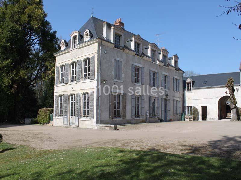 Grande maison ancienne à trois étages avec volets bleus, située dans une cour dégagée entourée de verdure.