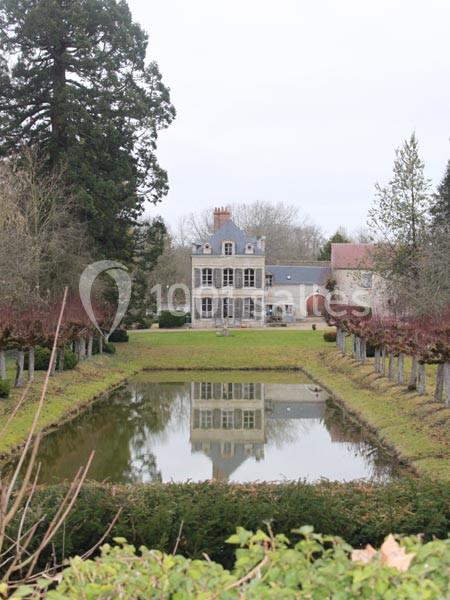 Manoir en pierre entouré de jardins, avec un bassin rectangulaire reflétant la façade et des arbres en arrière-plan.