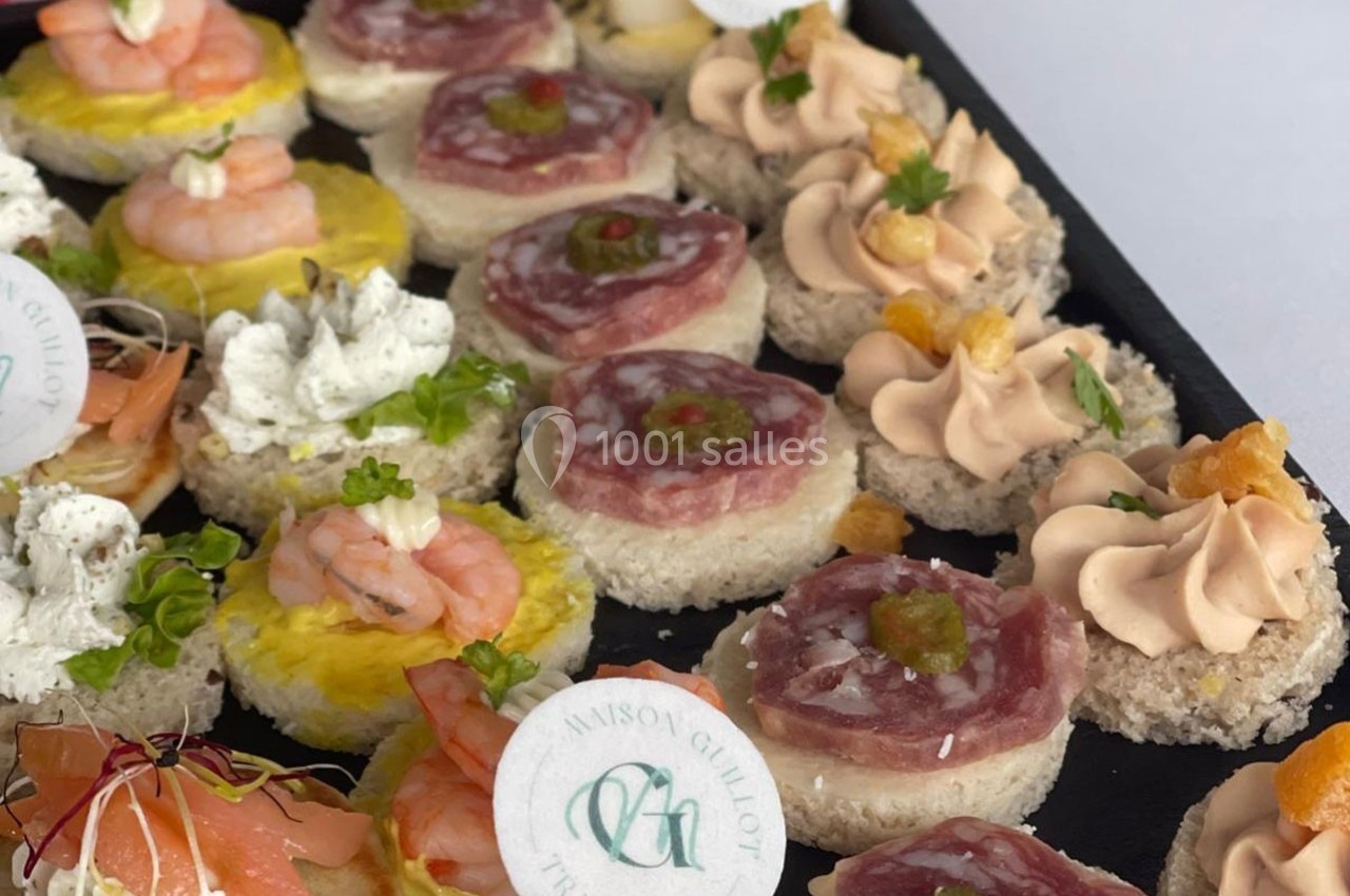 Plateau de canapés variés comprenant crevettes, mousse, charcuterie et garnitures décoratives.