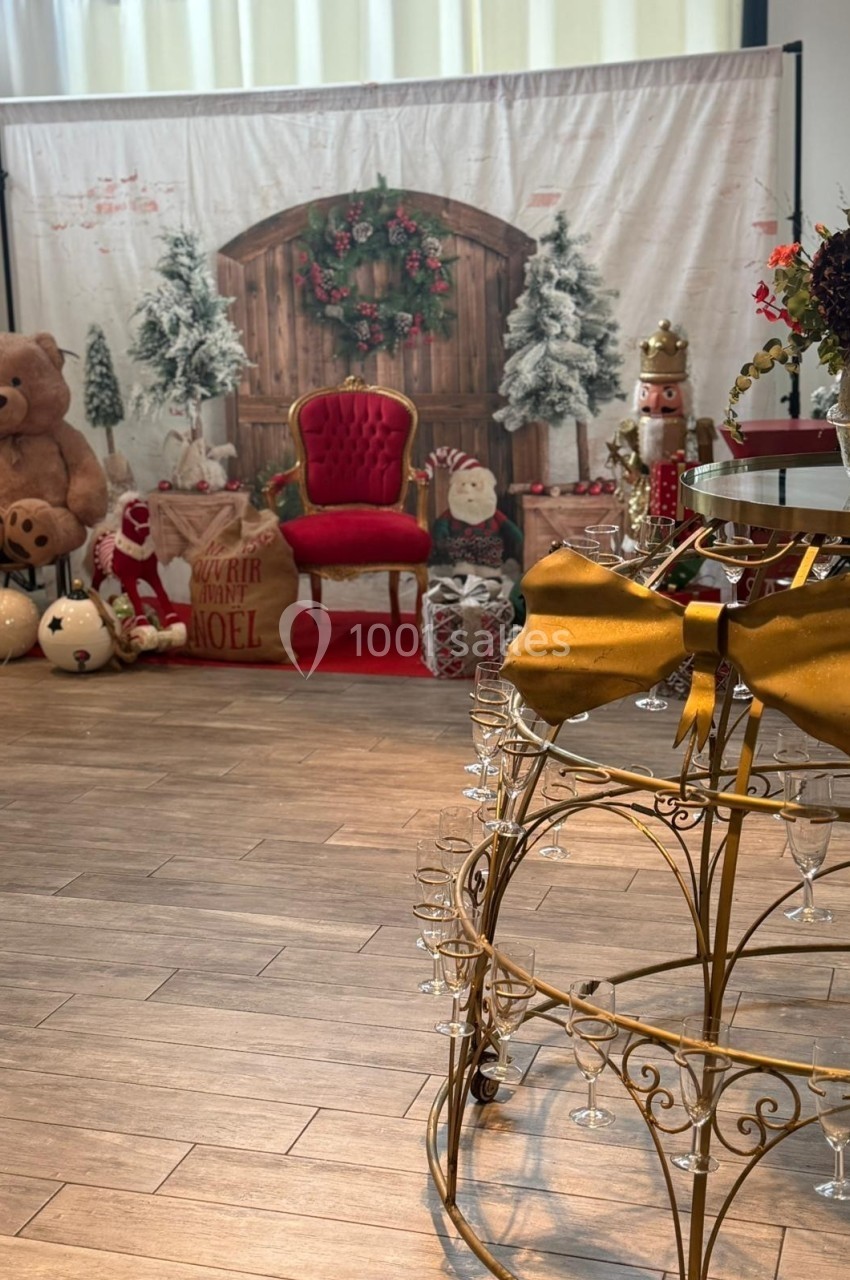 Décor de Noël avec fauteuil rouge, ours en peluche, cadeaux, sapins enneigés et table dorée ornée d'un nœud.