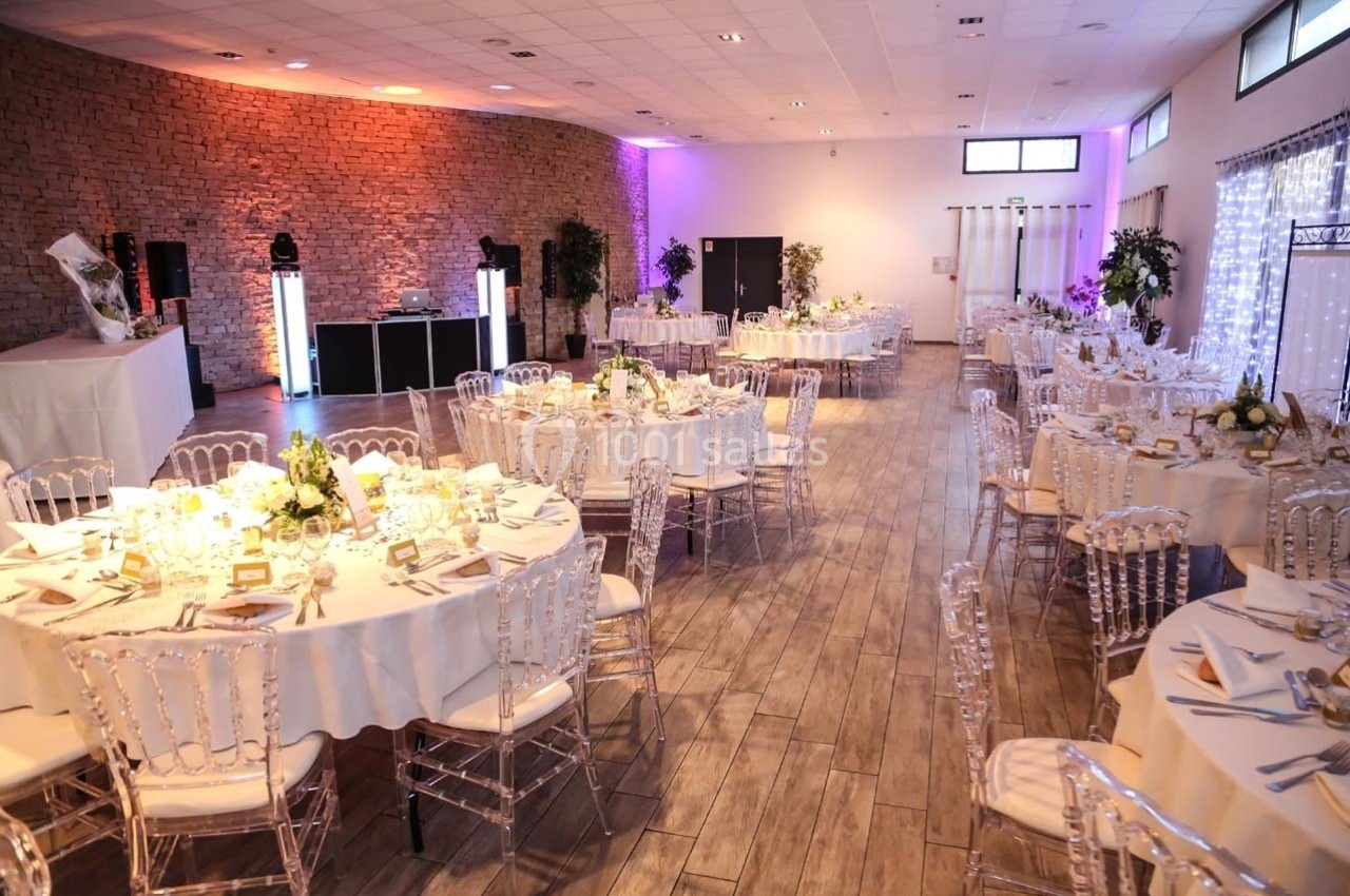 Salle de réception décorée avec des tables rondes dressées, des chaises transparentes et un éclairage tamisé.