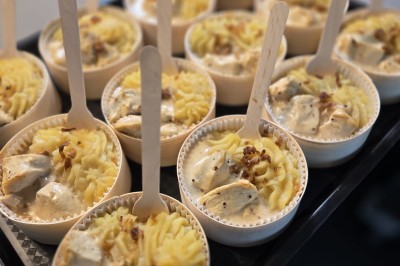 Petits plats individuels contenant purée, morceaux de viande en sauce et cuillères en bois, disposés sur un plateau.